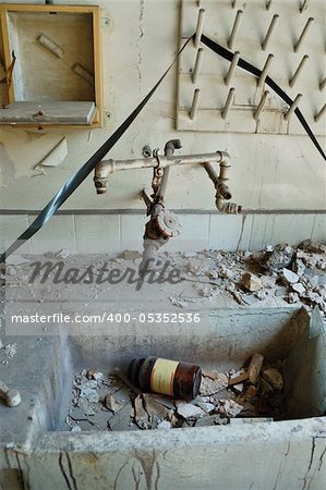 Dirty industrial sink with broken glass bottle of chemical substance and dusty audio reel tape in abandoned vinyl records pressing factory.