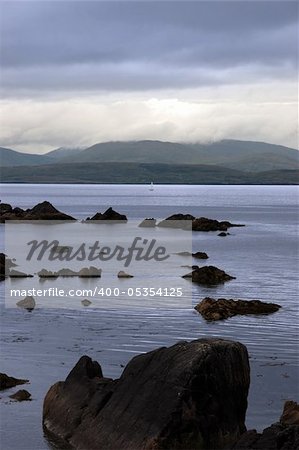 scenic view in kerry ireland of lone yacht sailing in  rocks and sea with mountains against a beautiful cloudy sky