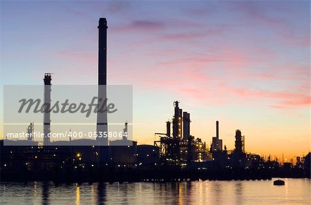 The silhouette of an oil refinery at sunset, against a radiant sky