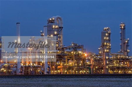 A petrochemical plant, with it's stainless steel cylinders, it's valves, chimneys, pipes, tubes and construction artificially lit just before the break of dawn
