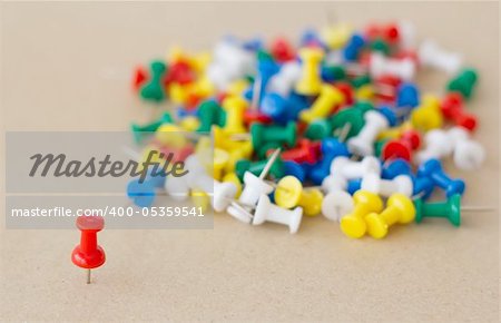 Collection of various pushpins on cork board with leading red pin