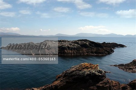 scenic view in kerry ireland of rocks and sea with mountains against a beautiful blue cloudy sky