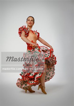 Young woman dancing flamenco with castanets on gray background