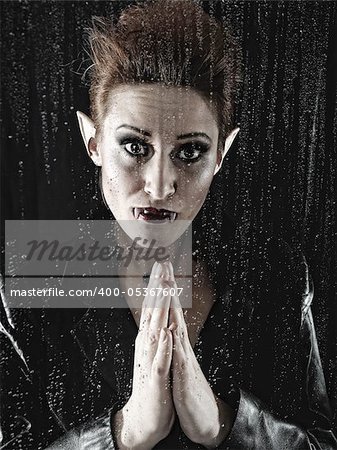 Funny Portrait of a beautiful fashion vampire woman behind rainy window
