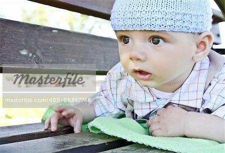 A cute little baby is looking   ahead and is wearing a blue hat. The baby is  a boy   and has dark eyes.