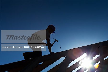 Builder or carpenter working on the roof - silhouette with strong back light