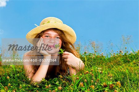 Young teenage girl laying in summer meadow resting chin on hand smelling flower