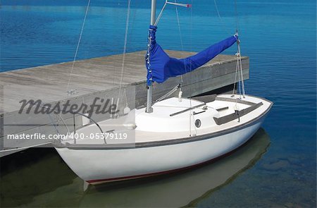 A small white boat waits at a wooden dock.