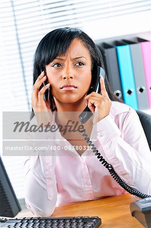 Young black business woman multitasking using two phones in office