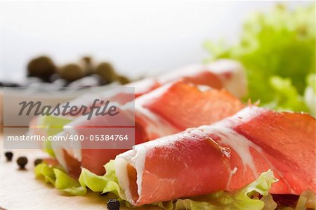 Slices of prosciutto rolled up and arranged on a lettuce leaf. Shallow depth of field.