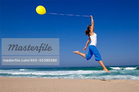 Beautiful and athletic Girl jumping with a balloon on the beach