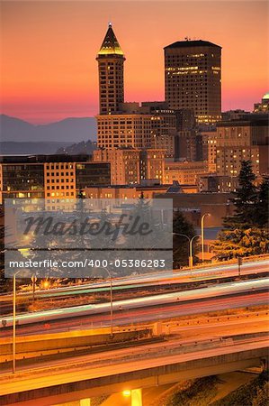 Seattle downtown buildings and Smith tower in the sunset glow with colorful streaks of traffic lights in the foreground freeways
