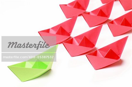 One green and several red paper boats on white background