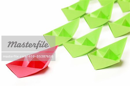 One red and several green paper boats on white background