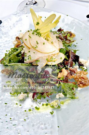 Beautifully plated fresh mixed green salad with pears, walnuts and goat cheese.  This salad is served on a glass plate.