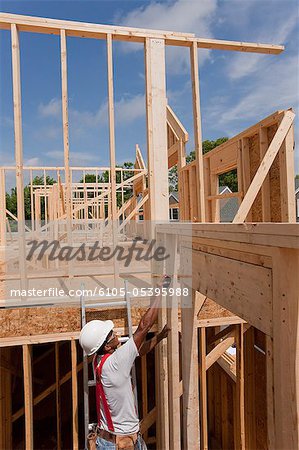 Hispanic carpenter taking a measurement of house framing