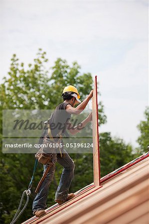 Hispanic carpenter carrying a particle board at a house under construction