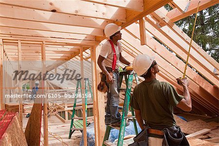 Hispanic carpenters using tape measure at a house under construction