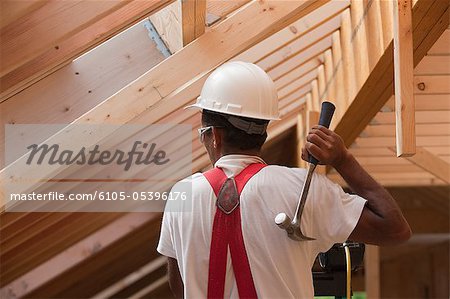 Hispanic carpenter using hammer on upper floor at a house under construction