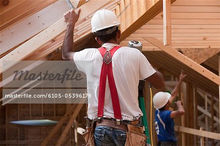 Hispanic carpenter using nail gun on upper floor at a house under construction