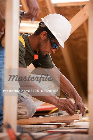 Charpentier hispanique marquant une mesure sur une planche dans une maison en construction