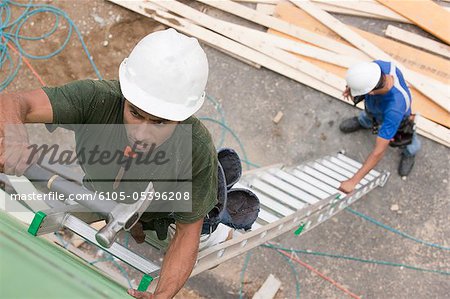 Carpenters on an extended ladder for installing sheathing at a construction site