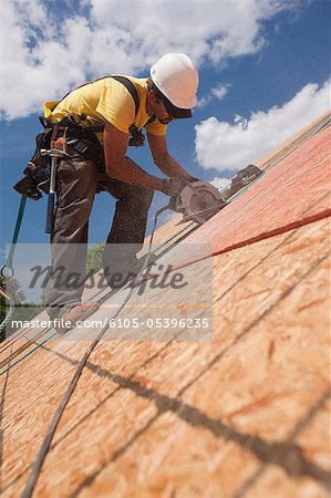 Charpentier à l'aide d'une scie circulaire sur le panneau de toit sur une maison en chantier