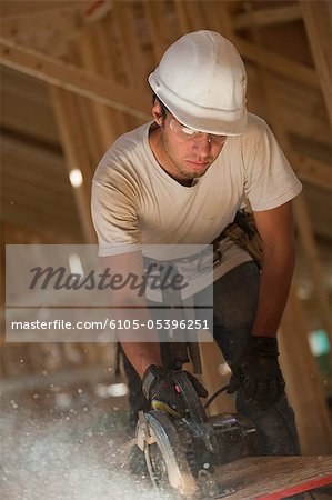 Carpenter using a circular saw on roof panel at a house under construction