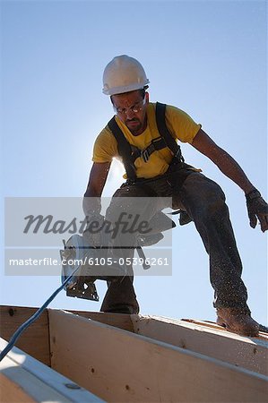 Hispanic carpenter using a circular saw on the roof beams at a house under construction