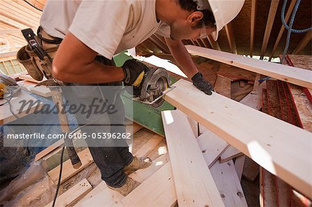 Hispanische Zimmermann mit einer Kreissäge auf einem Sparren ein Winkel-Haus im Bau