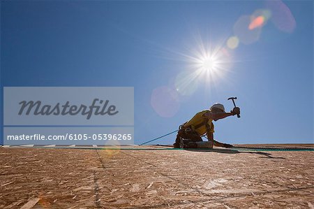 Hispanic carpenter using a hammer on the roofing at a house under construction