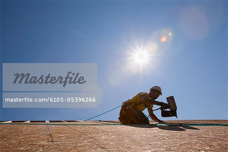 Hispanic carpenter using a nail gun on the roof of a house under construction