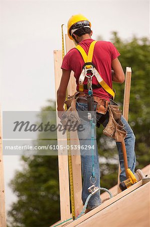 Charpentier hispanique mesurant la planche sur le toit d'une maison en construction