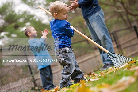 Boy raking leaves in a park with his father and brother communicating in American Sign Language