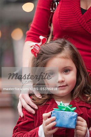 Portrait of a girl standing with her mother and holding a Christmas gift