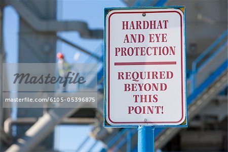 Warning sign saying 'Hardhat and Eye Protection Required Beyond This Point' at an industrial plant
