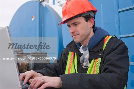 Engineer recording data on a laptop near a fuel tankers site