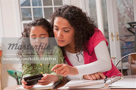 Hispanic woman helping her daughter to send a message on a mobile phone