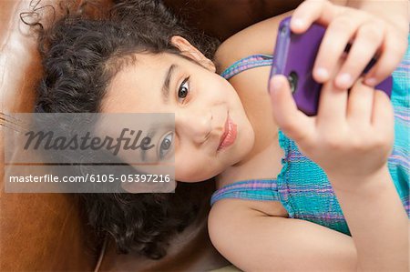 Hispanische Mädchen auf einer Couch liegen und Blick auf eine SMS-Nachricht auf einem Mobiltelefon