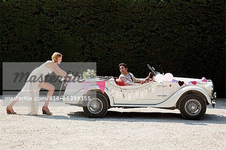 Bride pushing broken down vintage car