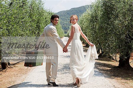 Les nouveaux mariés marchant sur une route de campagne avec valise