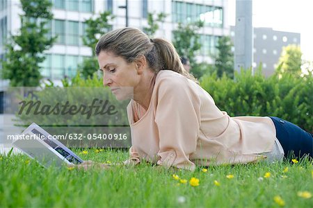 Woman lying in grass reading book
