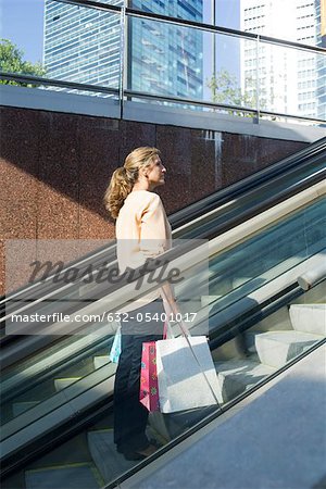 Frau trägt Einkaufstaschen hinauf auf Rolltreppe im freien