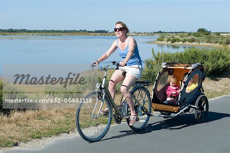 Woman riding along bicycle path with children in bicycle trailer