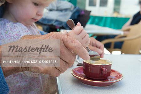 Toddler girl helping grandmother stir cup of coffee, cropped