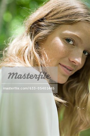 Jeune femme souriante par-dessus l'épaule à la caméra, portrait