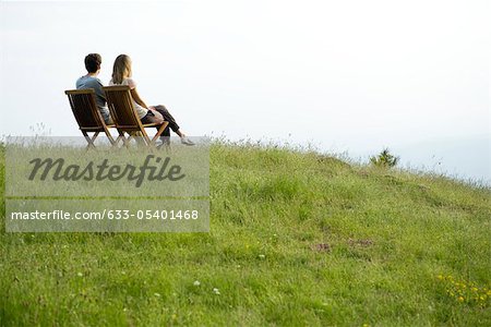 Couple assis sur des chaises au sommet de la colline regardant vue