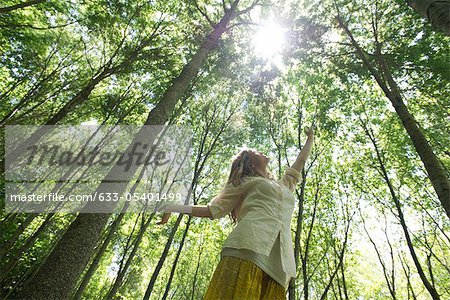 Jeune femme debout dans les bois, atteignant vers le soleil qui brille à travers la canopée