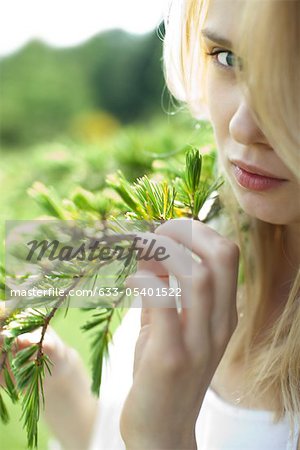 Young woman holding pine needle branch, cropped