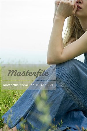 Young woman sitting in meadow, hands under chin, cropped